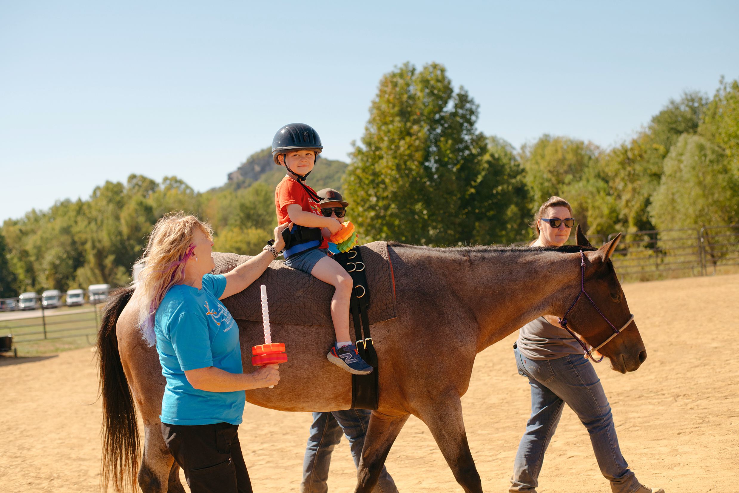 Child riding a horse with therapists walking alongside.
