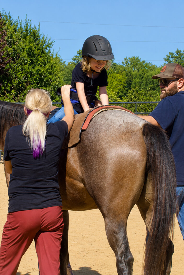 Child riding a horse backward with therapists alongside